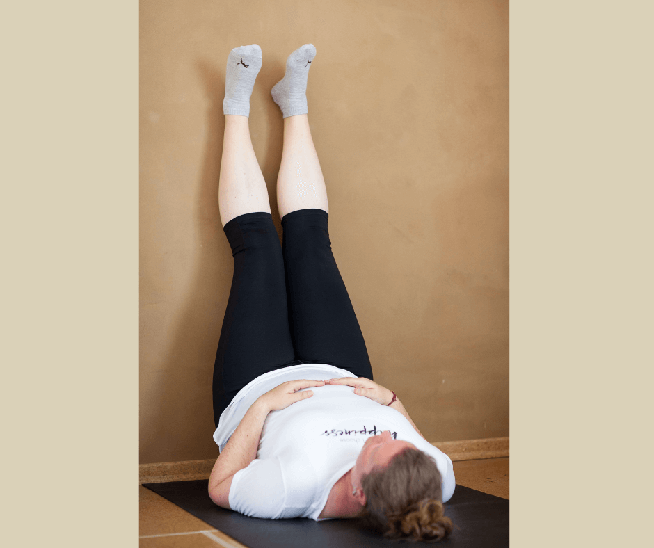 kurvige Frau in Yogakleidung liegt auf dem Rücken und lehnt die gestreckten Beine an die Wand